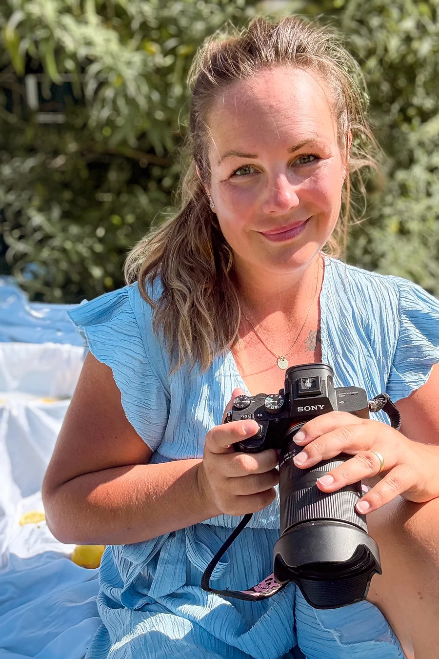 Bianca sitzt draußen im Sommerlicht und lächelt, ihre Kamera in den Händen
