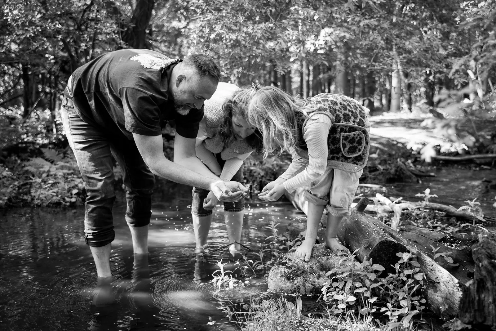 Schwarzweißbild: Eltern spielen mit ihrem Kind an einem Bach im Wald