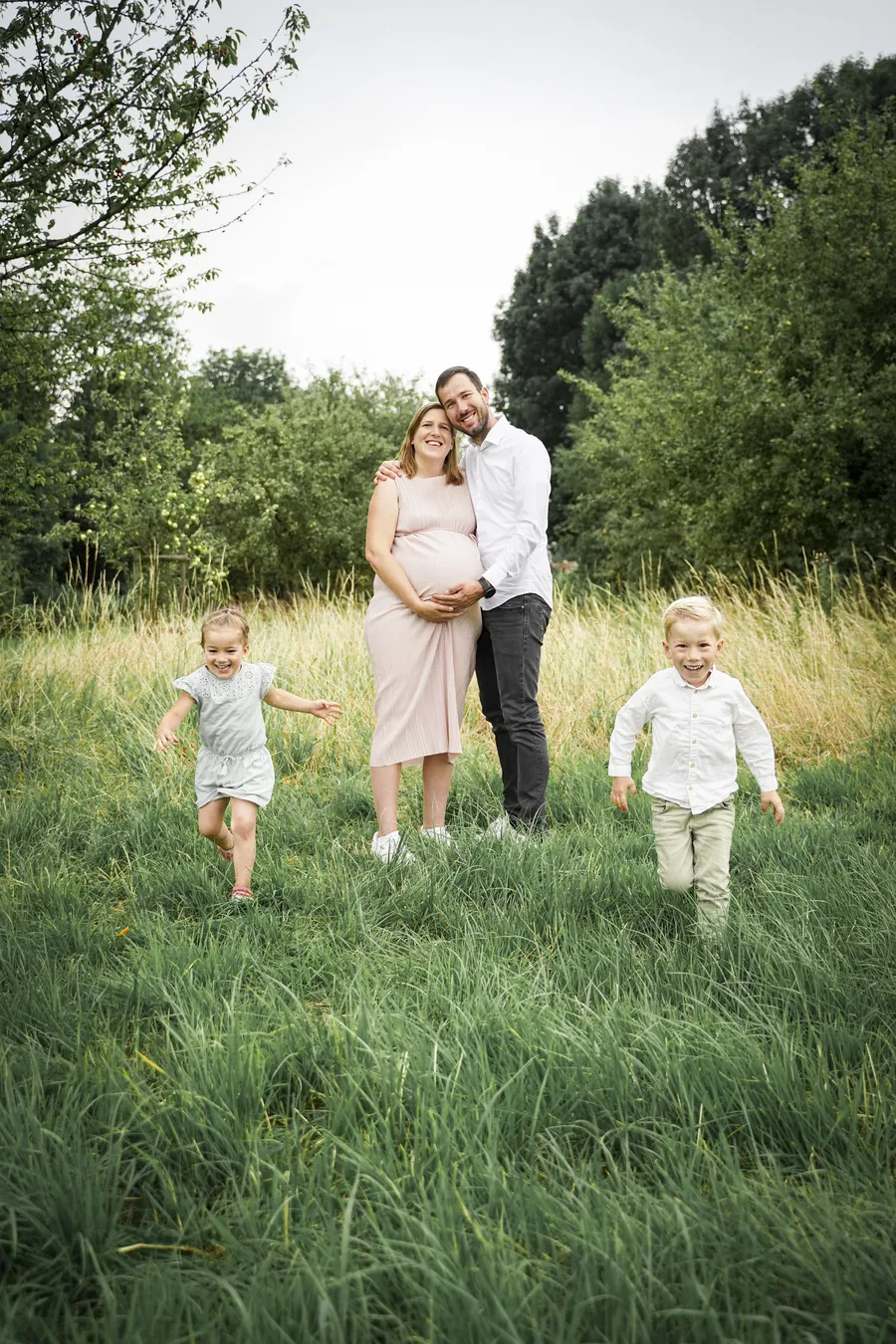 Eine schwangere Frau geht mit ihrem Partner und zwei Kindern über eine grüne Wiese