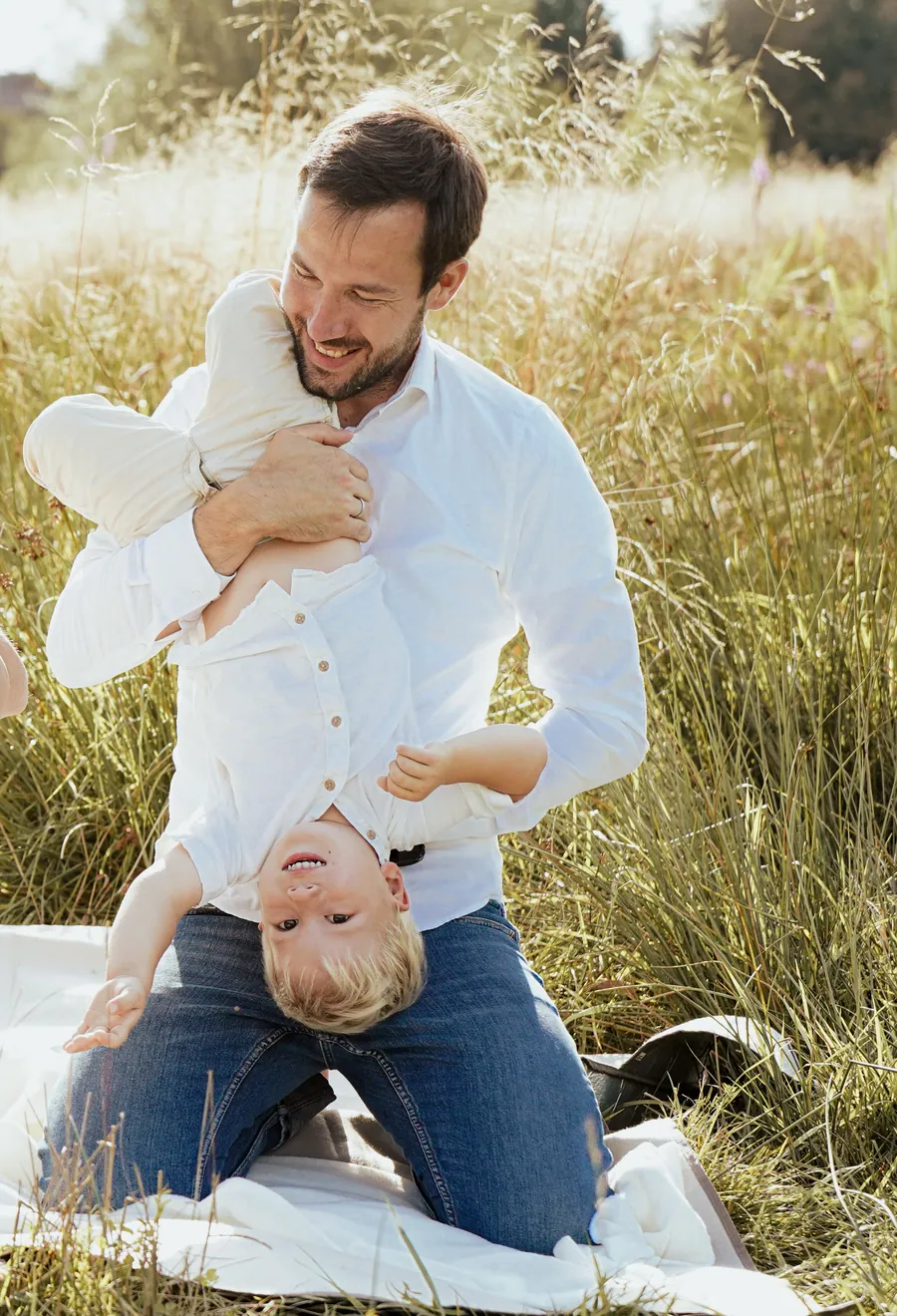 Ein Vater hält sein Kind spielerisch kopfüber auf einer Sommerwiese