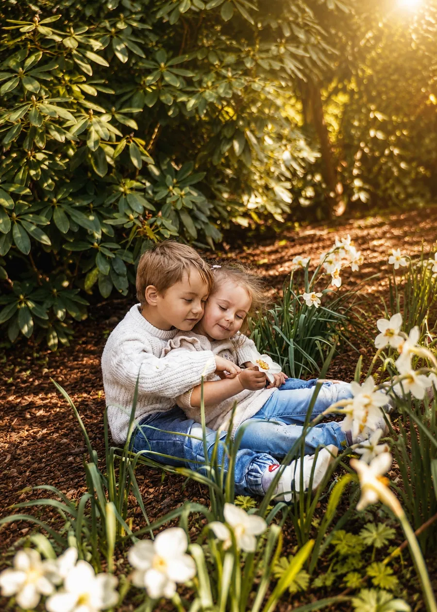 Zwei Kinder liegen im warmen Abendlicht zwischen blühenden Narzissen