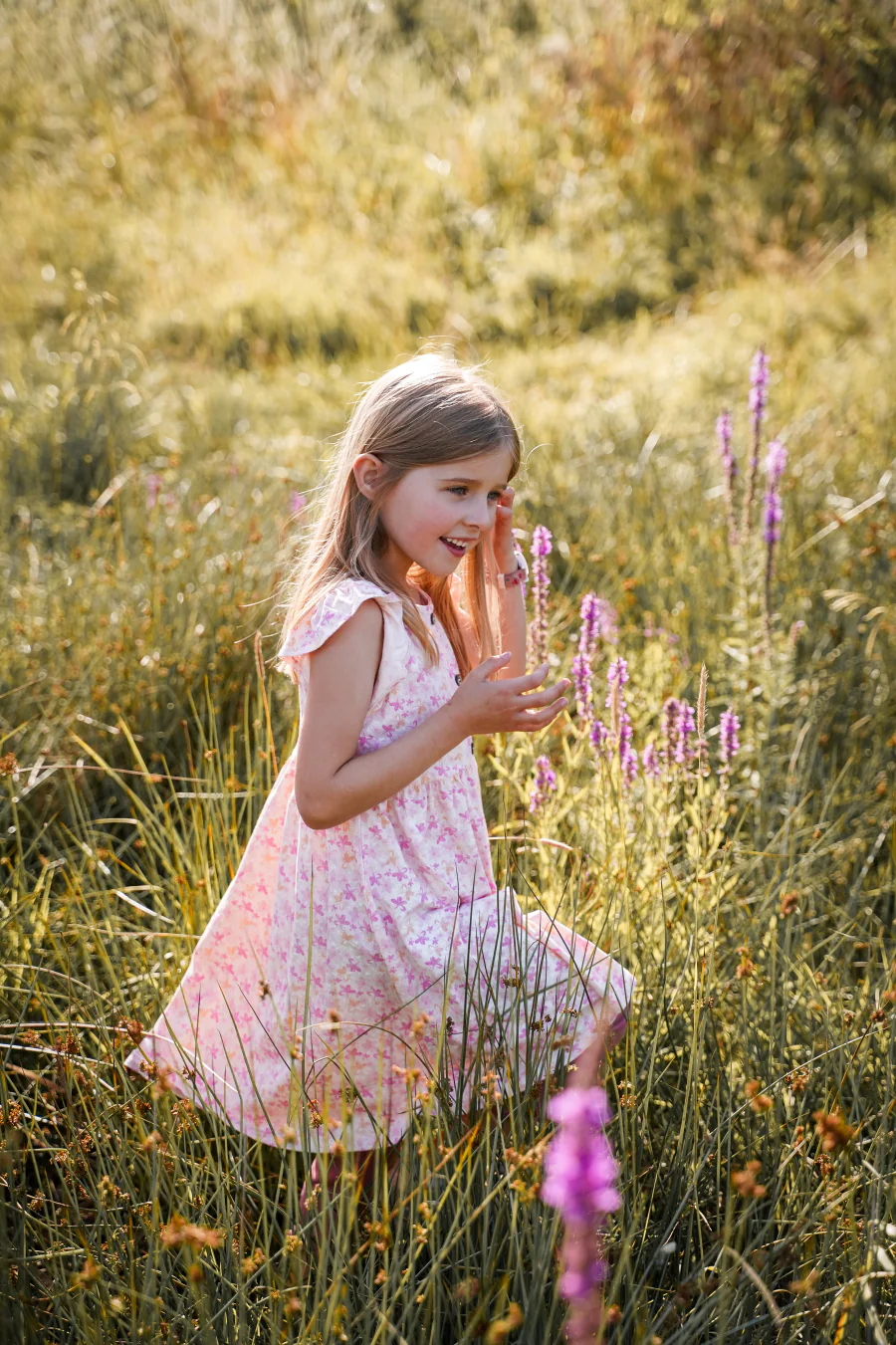 Ein Mädchen im geblümten Kleid geht durch eine sommerliche Wiese