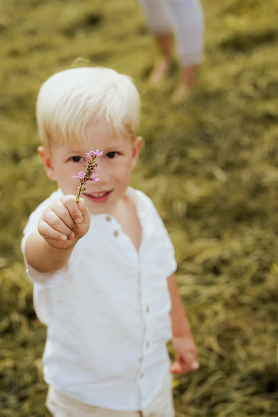 Ein kleiner Junge hält lächelnd eine winzige Blume in die Kamera