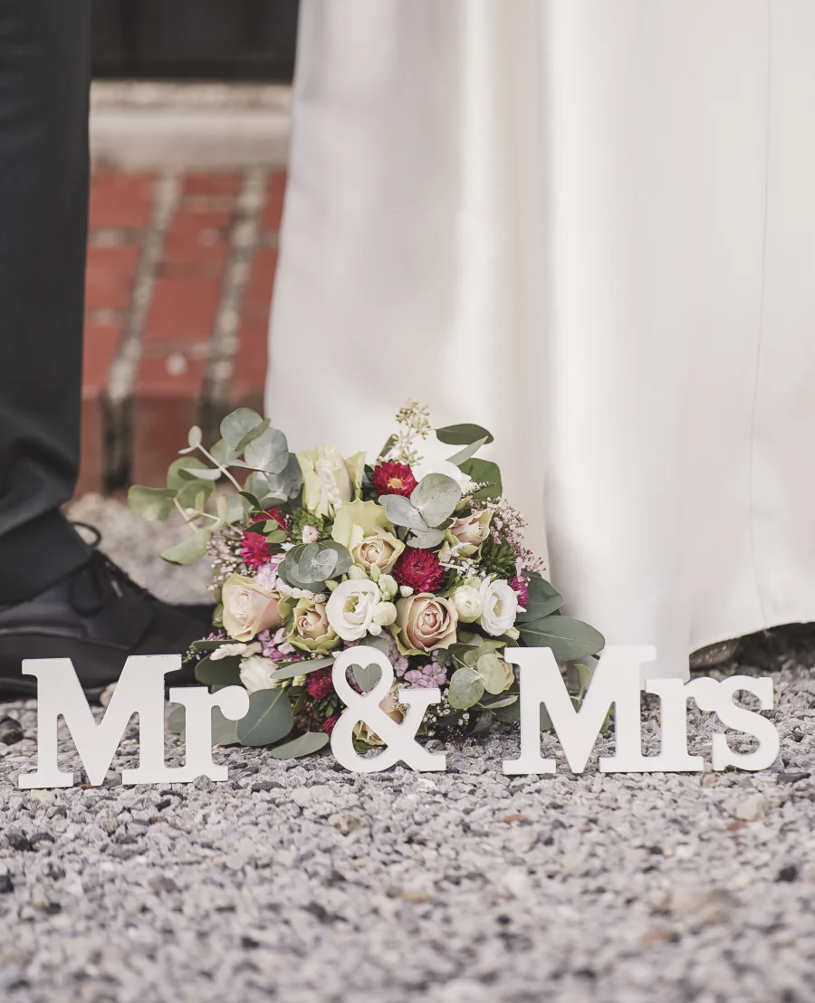Ein Brautstrauß steht zwischen den Buchstaben Mr und Mrs auf einer Steinbank