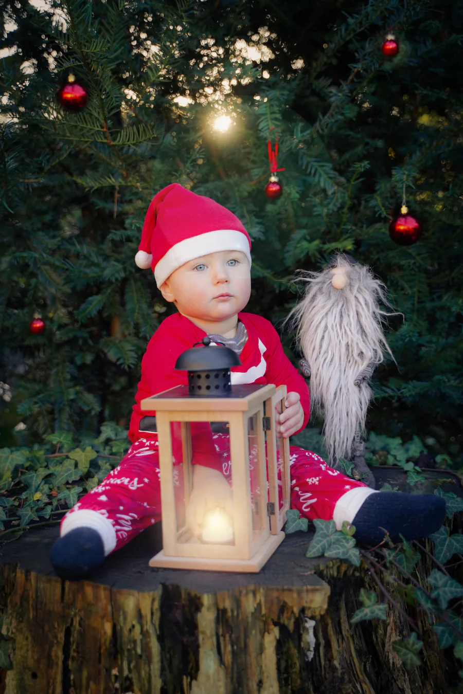 Ein Kleinkind mit roter Weihnachtsmütze sitzt neben einer leuchtenden Laterne