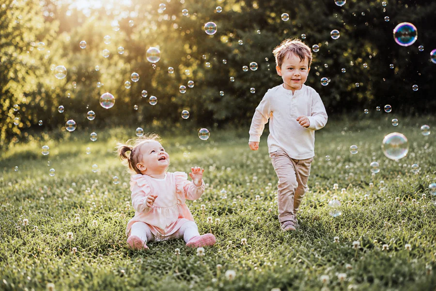Zwei kleine Kinder spielen im warmen Abendlicht zwischen vielen Seifenblasen