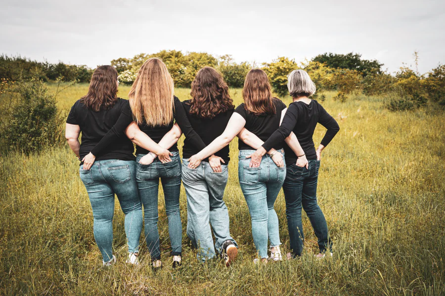 Fünf Frauen gehen Arm in Arm durch eine weite Wiese, von hinten fotografiert