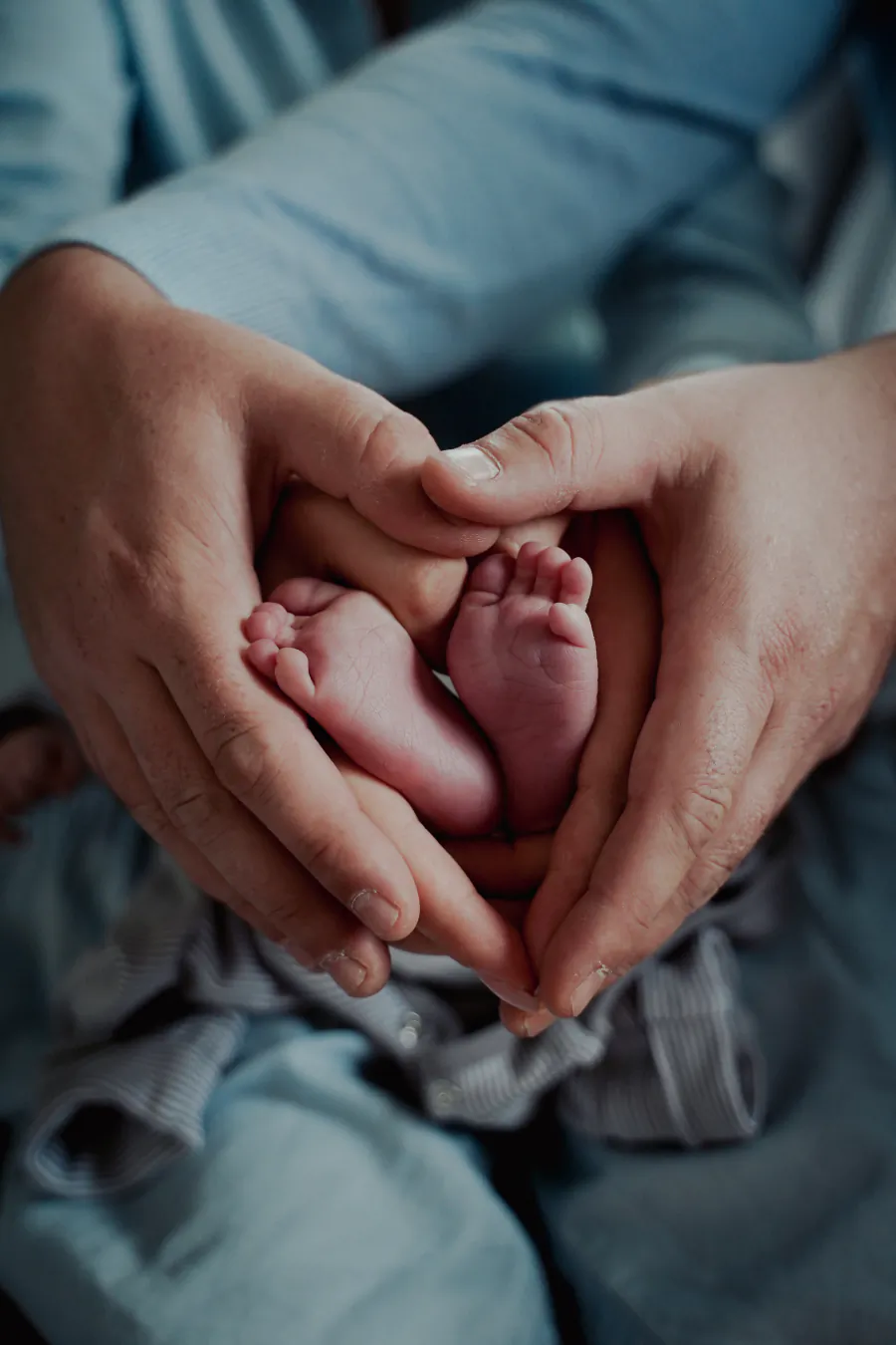 Nahaufnahme: Die Füße eines Babys liegen in den Händen zweier Erwachsener