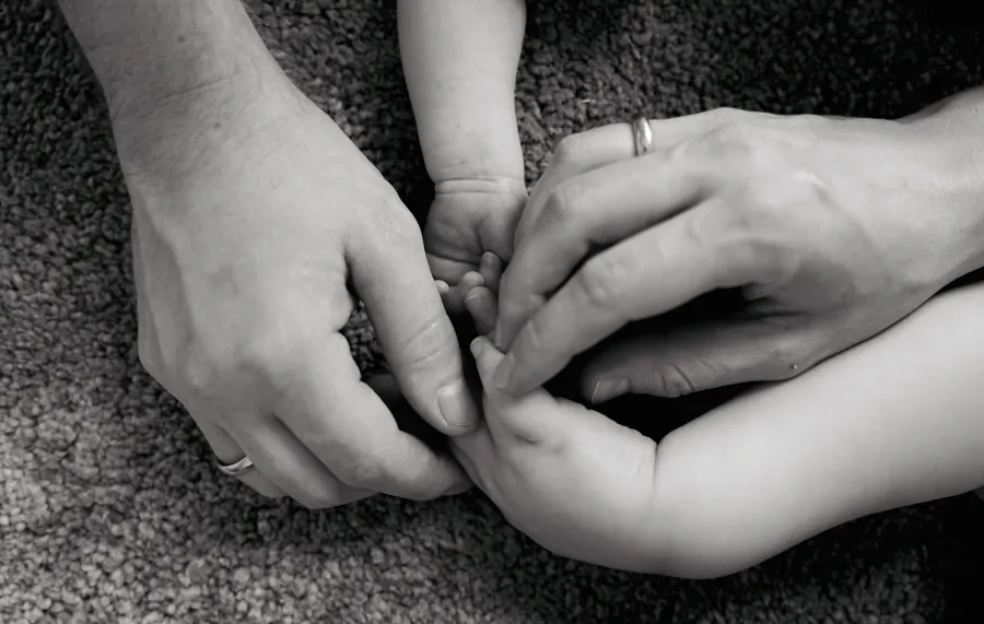 Schwarzweißbild: Erwachsene Hände und Kinderhände berühren gemeinsam die Hand eines Babys