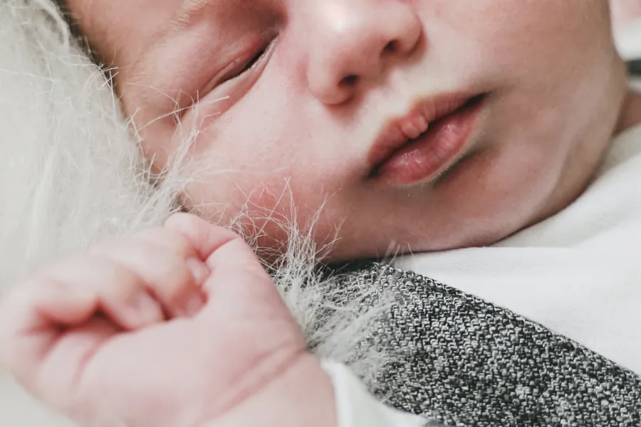 Nahaufnahme: Ein schlafendes Baby liegt mit der Hand an der Wange