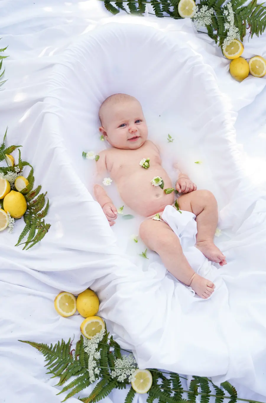 Ein Baby liegt zwischen Zitronenscheiben und grünen Zweigen in einem hellen Milchbad