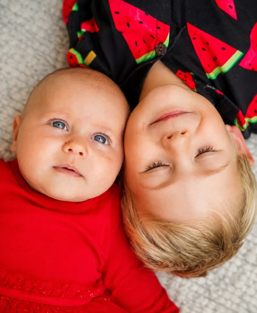Ein Baby liegt neben einem älteren Kind, beide tragen rot-schwarze Kleidung