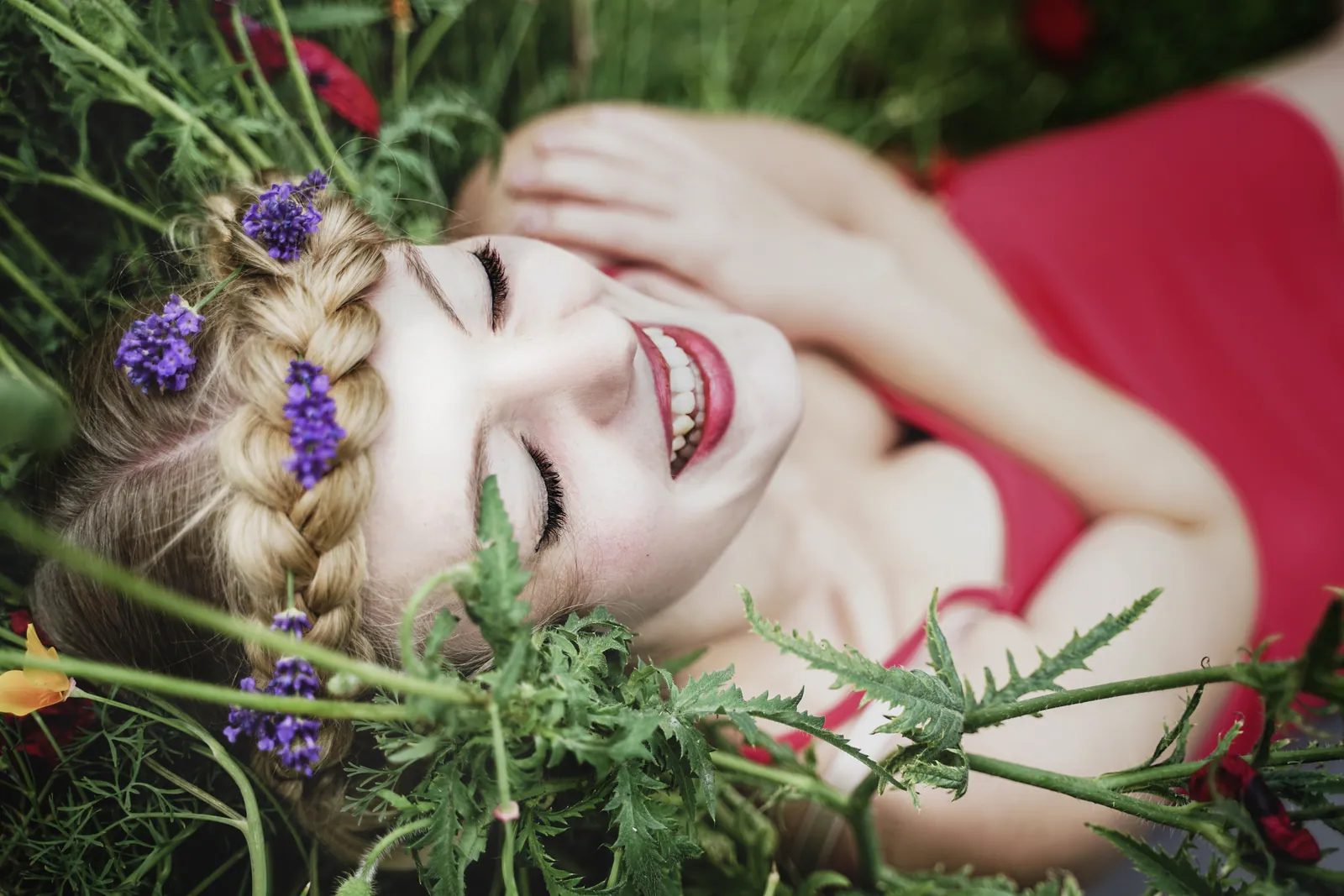 Eine Frau mit Blumen im geflochtenen Haar liegt lachend in einer Blumenwiese