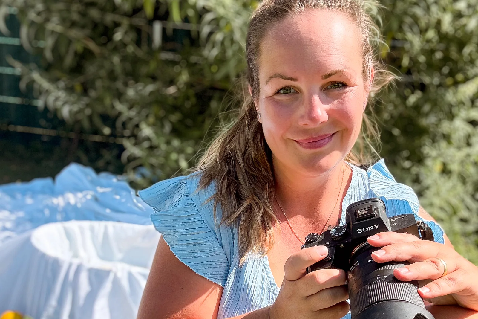 Bianca sitzt draußen im Sommerlicht und lächelt, ihre Kamera in den Händen