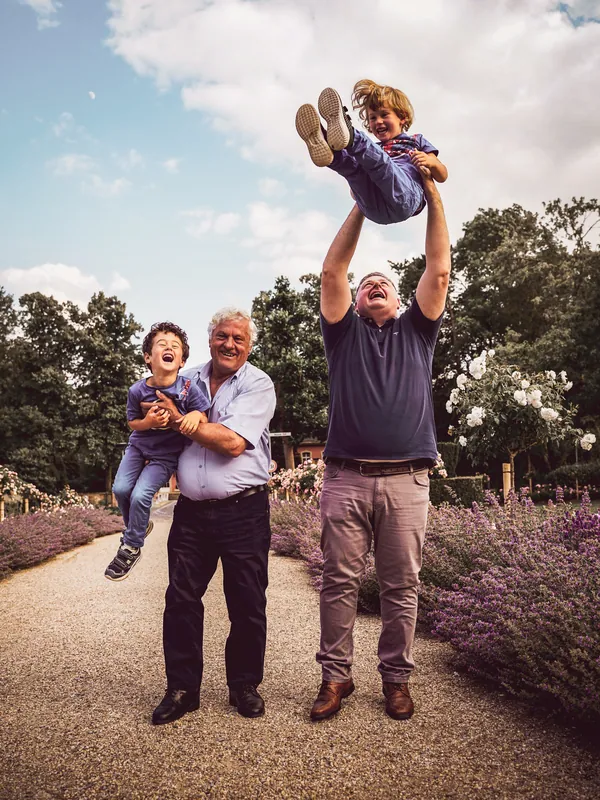 Ein Mann hebt ein lachendes Kind hoch in die Luft, daneben hält ein Großvater einen Jungen im Arm